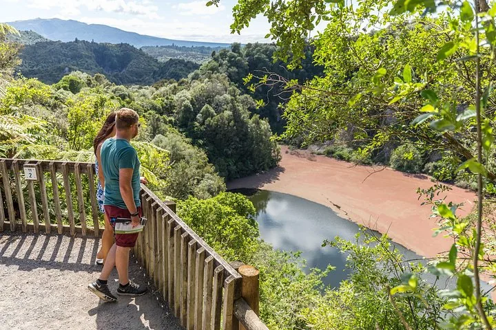 Zwei Touristen stehen auf einer Aussichtsplattform und blicken auf einen grünen und braunen See.
