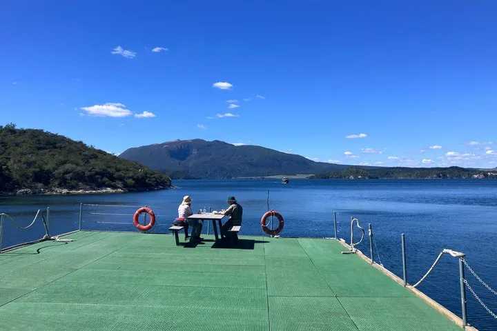 Twee mensen zitten aan een picknicktafel op een steiger met uitzicht op een meer