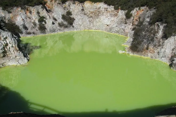 Leuchtend limettengrüner geothermischer Pool, umgeben von felsigen Klippen im Waimangu Volcanic Valley.
