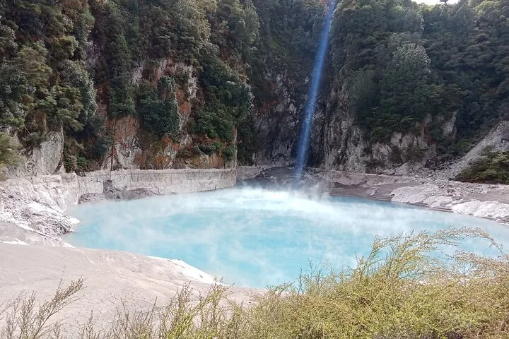 Gran lago geotérmico humeante de color azul pálido en un cráter rocoso del Valle Volcánico Waimangu