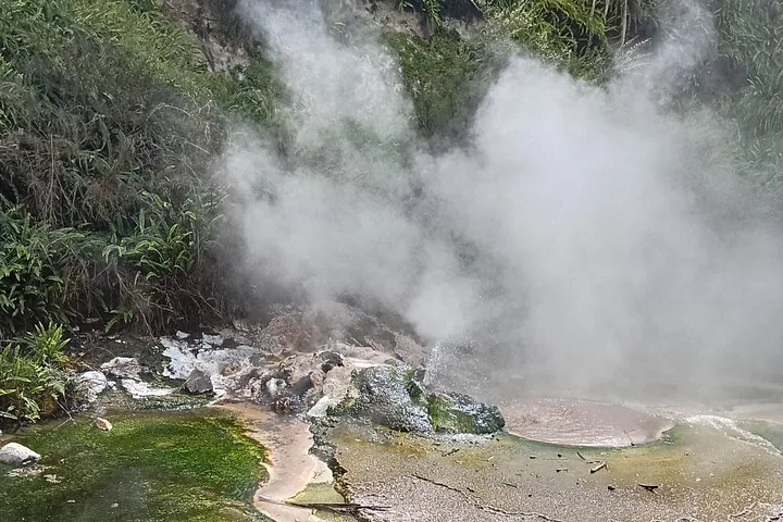 Vapor que se eleva en nubes de una fuente termal geotérmica rocosa con depósitos minerales de colores